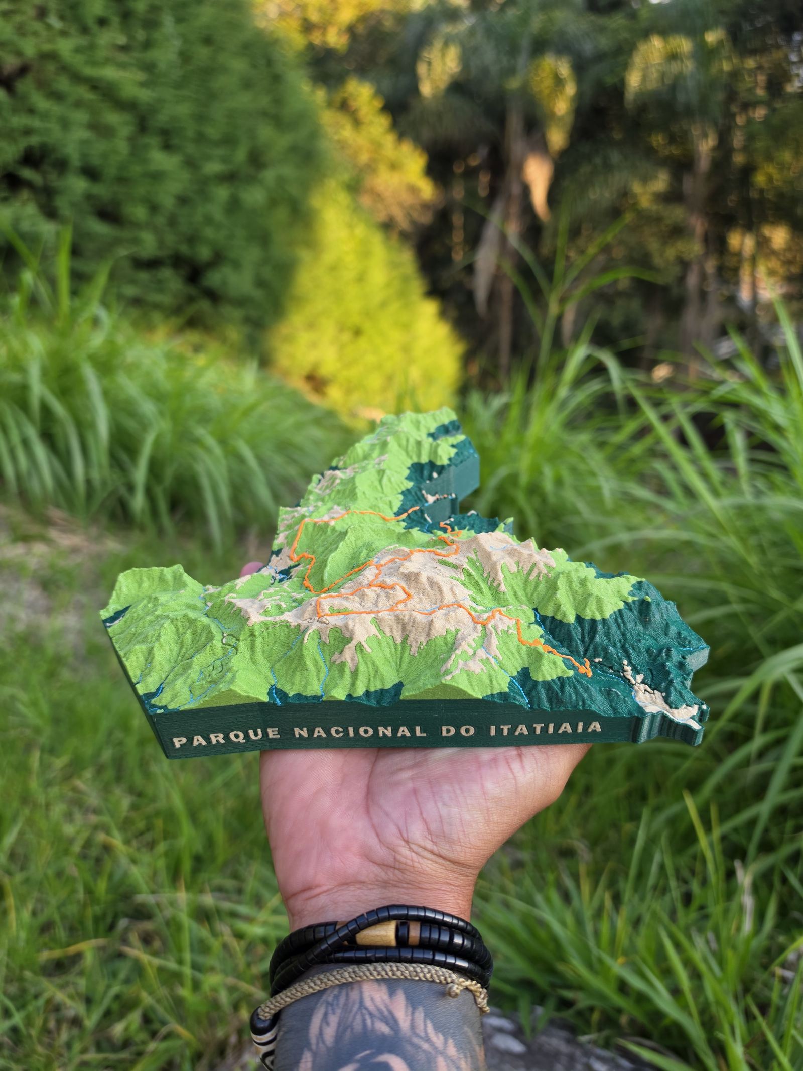 Maquete topográfica do Parque Nacional do Itatiaia segurada diante da vegetação da serra